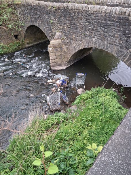 Stone bridge above a stream with shopping trollies in the water.